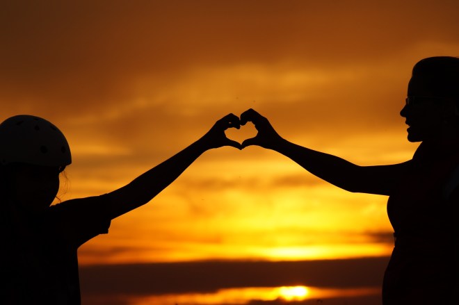 silhouette of 2 people forming heart with extended hands