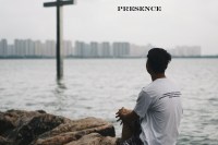 person comtemplatin cross with bay and city in background