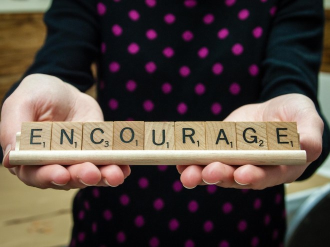 holding scrabble tiles spelling encourage