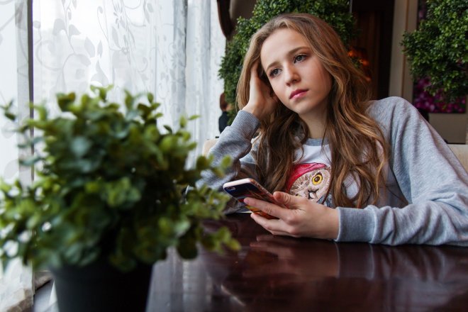 young girl leans head on hand staring into space, flowers window table
